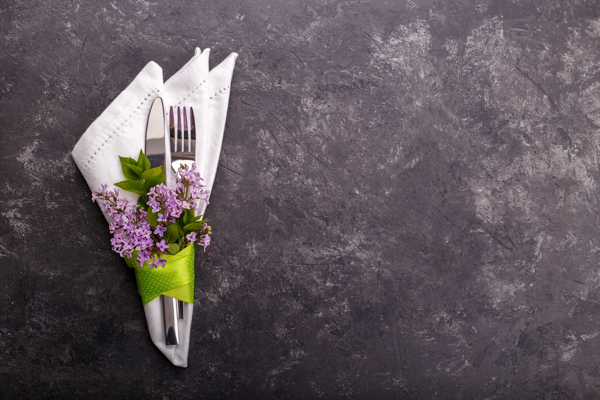 Spring festive table setting with cutlery and lilac flowers on black stone table,copy space flat lay