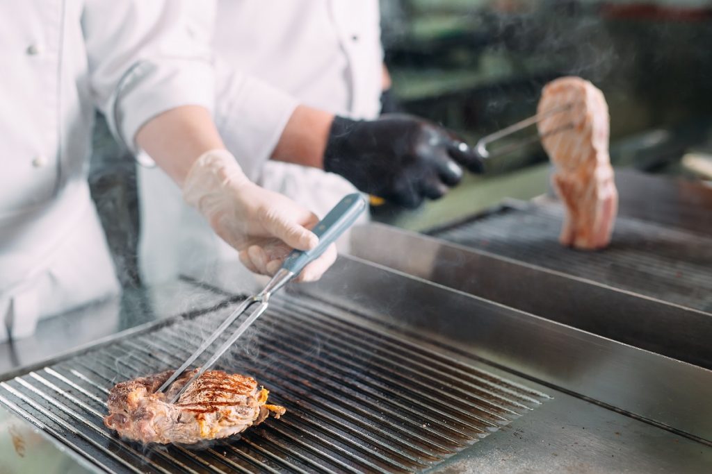 Cooks roast meat on the stove in the kitchen of a restaurant or